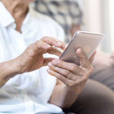 Das Bild zeigt eine ältere Person mit einem Mobiltelefon beim Suchen wichtiger Kontaktadressen.